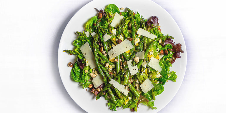 Eiwitrijke aspergesalade met rode biet, geitenkaas, ei en rucola op wit bord